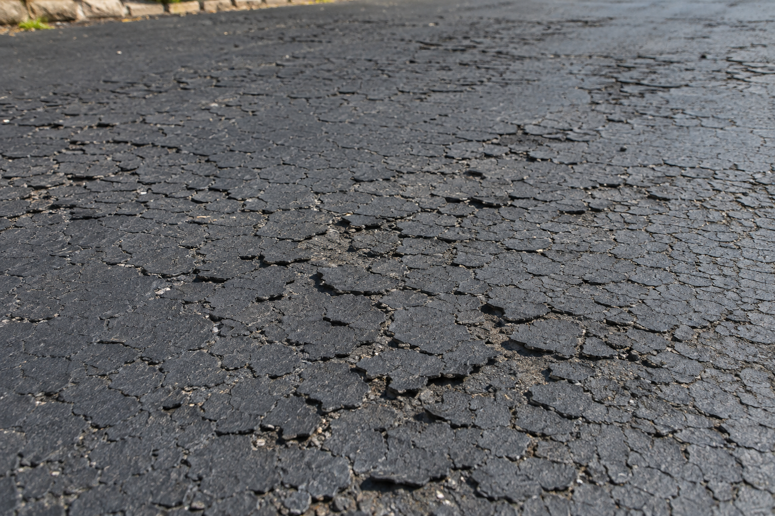 Over-sealed asphalt driveway with brittle cracked and flaking sealcoat from resealing too often in Springfield MO